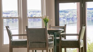 Een eethoek met een tafel en vier stoelen, een vaas met bloemen en uitzicht op een meer door grote ramen.