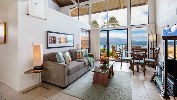 A spacious living area with a large window overlooking a scenic view, a ceiling fan, and a cozy seating arrangement. - Maui beachfront, steps to the sand!*Hono Kai C1* (Wailuku)