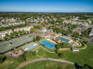 An aerial view of a residential area with houses, a tennis court, and a swimming pool.