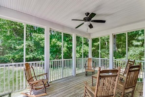 Une véranda couverte avec un plancher en bois, des balustrades blanches et un ventilateur de plafond.