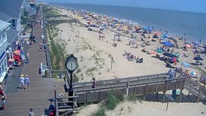 A beach with a wooden boardwalk, a clock, and a sandy shore with umbrellas.