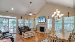 A spacious living room with a fireplace, a ceiling fan, a television, and a dining area with chairs.
