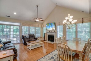 A spacious living room with a fireplace, a ceiling fan, a television, and a dining area with chairs.