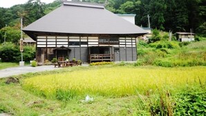 A traditional Japanese building with a tiled roof and wooden walls, surrounded by a lush green field. - Yukiwariso (Otari)
