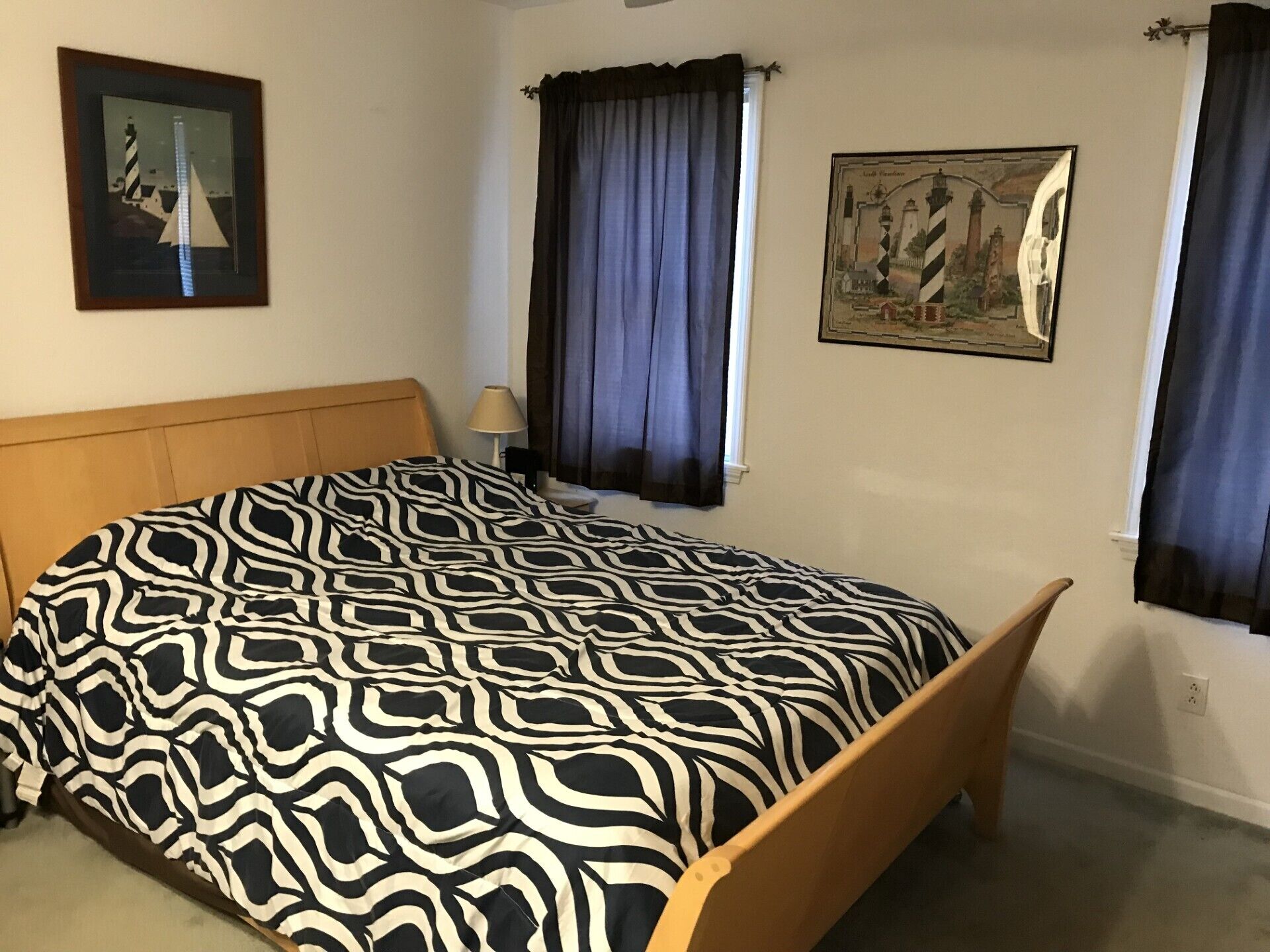 A bedroom with a patterned bedspread, a wooden headboard, a nightstand with a lamp, and two framed pictures on the walls.