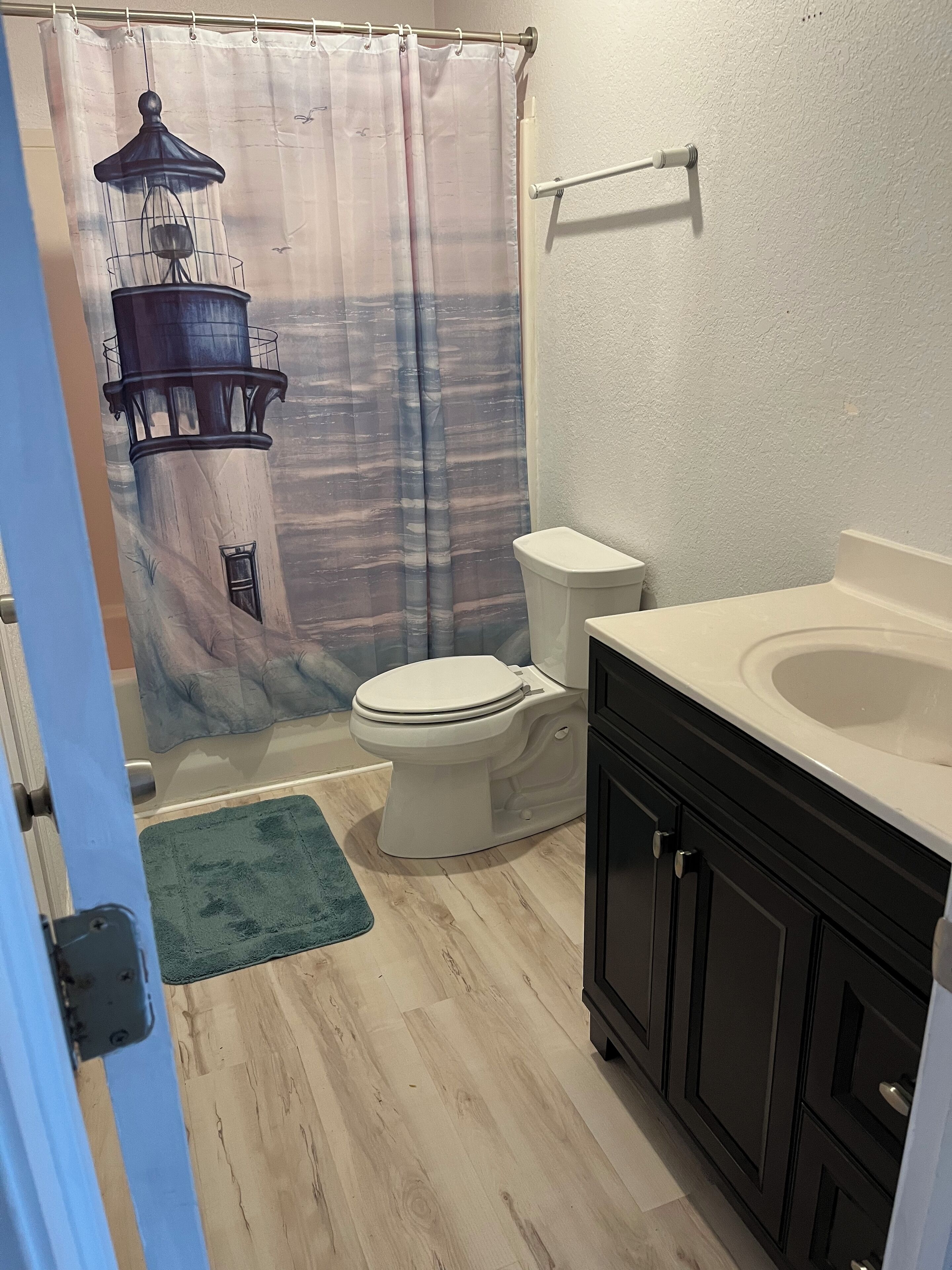 A bathroom with a toilet, a sink, and a shower curtain with a lighthouse design.