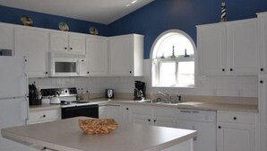 A modern kitchen with white cabinets, a central island, and a large window. - Don't Miss Out on the 'Sunshine'; Unwind, Relax, Put Your Feet Up and enjoy! (Kill Devil Hills)
