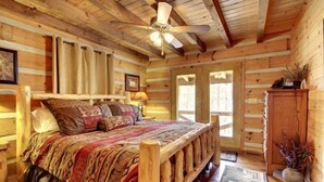 A log cabin bedroom with a wooden bed, a ceiling fan, and a view of the outdoors. - Perfect Getaway Lots 2 Do! Upscale Real-Log Cabin & Great Rate! Families/Couples (Blue Ridge)