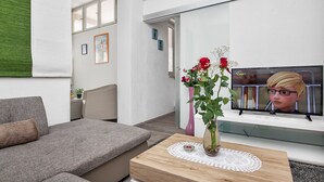 A modern living room with a grey sofa, a wooden coffee table with a vase of flowers, and a television on a white stand.
