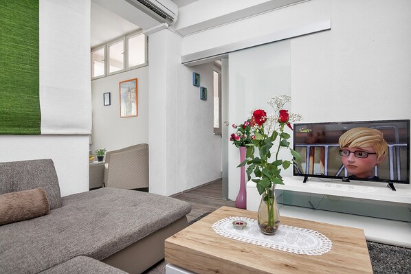 A modern living room with a grey sofa, a wooden coffee table with a vase of flowers, and a television on a white stand.