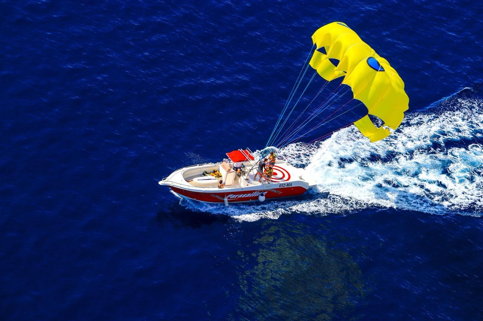 Un bateau avec une voile de traction, une personne portant un gilet de sauvetage et une autre personne portant une casquette rouge.