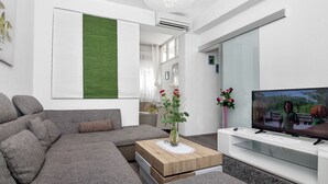 A modern living room with a grey sectional sofa, a wooden coffee table with a vase of flowers, a flat-screen TV, and a white entertainment unit.