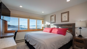 A bedroom with a large bed, a desk, a chair, a nightstand, and a window with a view of the landscape. - Ski-in, Walk-out, Views of Ski Slopes, Indoor Pool, Discount Lift Tix (Steamboat Springs)