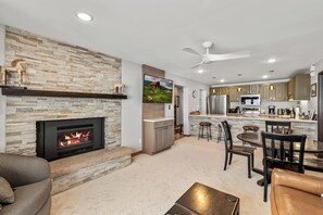 A modern living room with a fireplace, a dining area, and a kitchen with a bar.