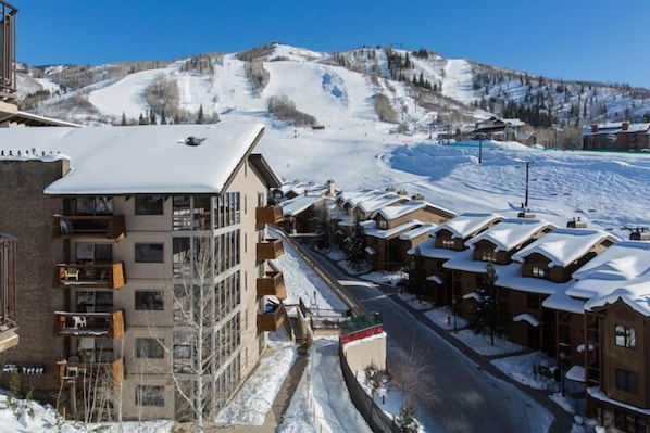 A ski resort with a building featuring balconies and a view of a snowy mountain slope.