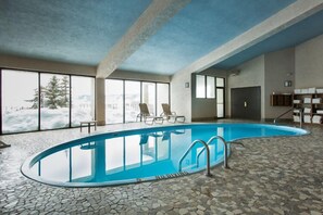 An indoor swimming pool with a tiled floor, large windows, and a view of a snowy landscape.