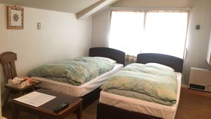 A small, well-lit room with two single beds, a wooden table with a remote control, a small chair, and a window with curtains. - Fujiyoshi (Nozawaonsen)