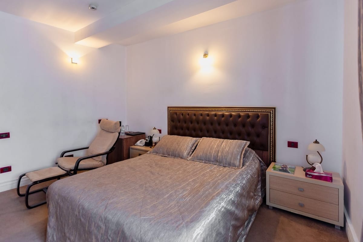 Una habitación de hotel con cama, una silla, una mesita de noche y una lámpara.