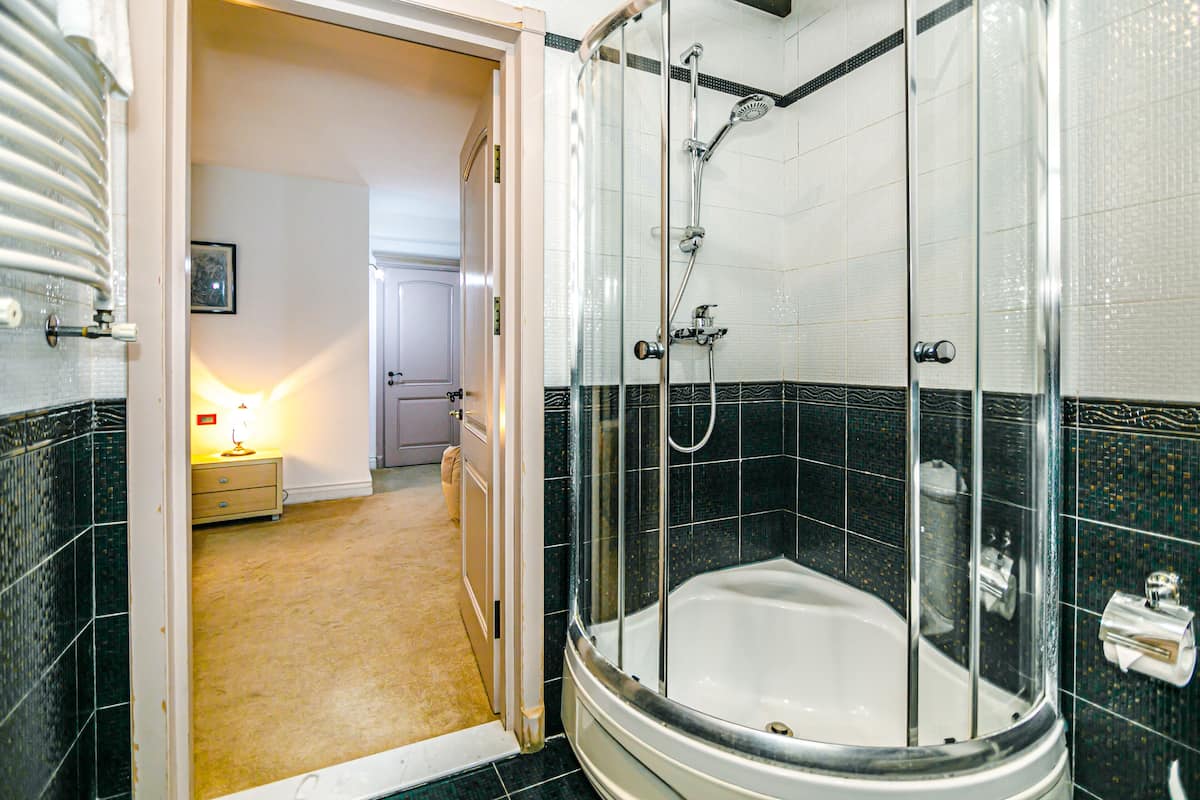 Un baño con ducha envuelta en cristal, una bañera blanca y paredes de baldosas oscuras.
