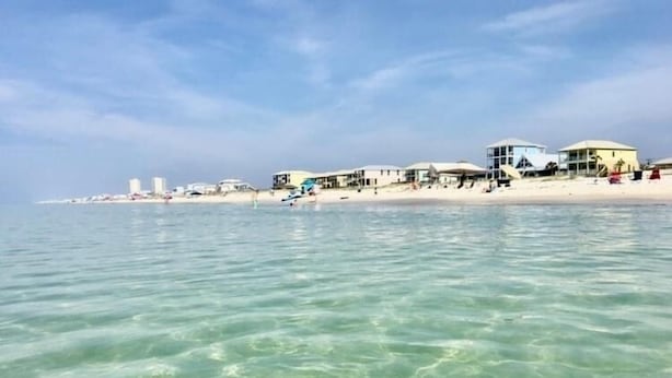 Ein Strandhotel mit mehreren Gebäuden direkt am Ufer, klarem türkisblauem Wasser und einem Sandstrand.