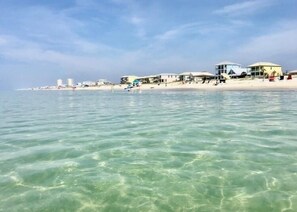 Un hotel frente a la playa con varias edificaciones a lo largo de la costa, agua turquesa cristalina y una playa de arena.