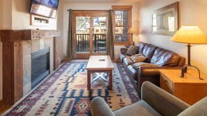 A living room with a fireplace, a sofa, a coffee table, and a TV mounted on the wall. - 8884 | Springs, wood floors, steps to gondola! (Keystone)
