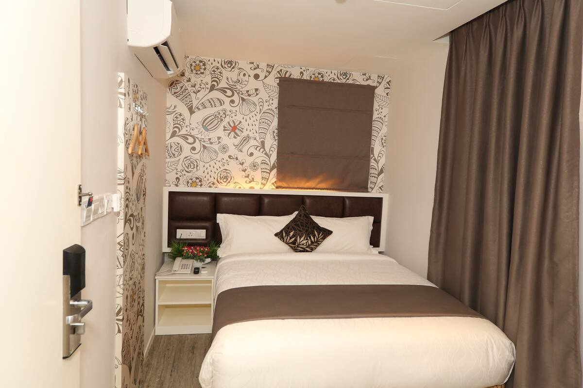A neatly arranged hotel room with a bed, bedside table, and a wall-mounted air conditioning unit.
