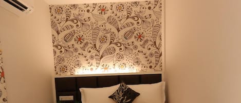 Cama bem arrumada com cabeceira, mesa de cabeceira com abajur e parede com padrão floral.