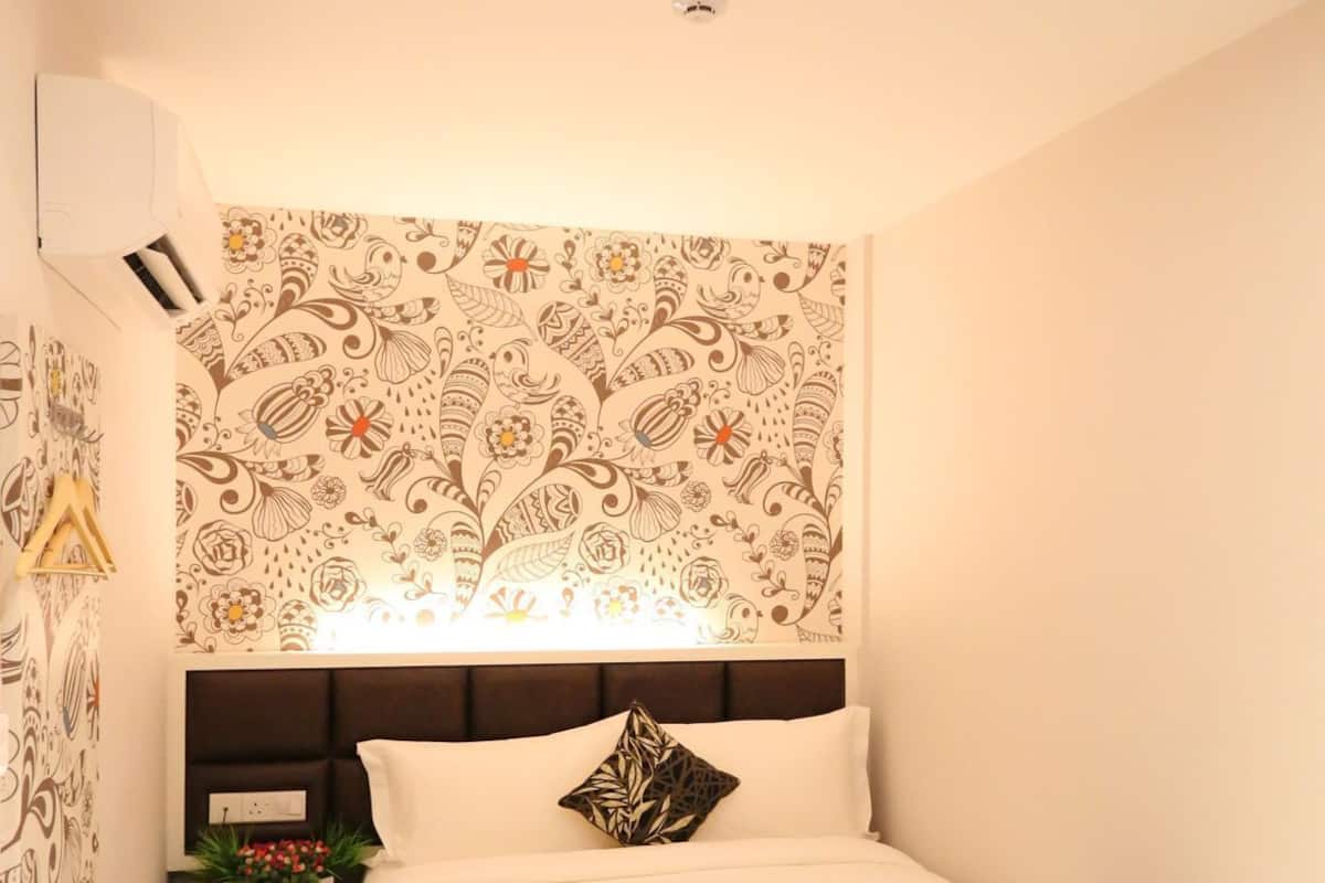 A hotel room with a bed, a nightstand, a wall-mounted air conditioner, and a patterned wall.