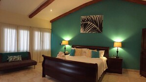 A bedroom with a large bed, two bedside tables with lamps, a sofa with a green throw, and a wall art piece. - Perfect Location, Walk to Beach, Infinity Pool, Luxury Decor, Fast Free Wifi! (Dominical)