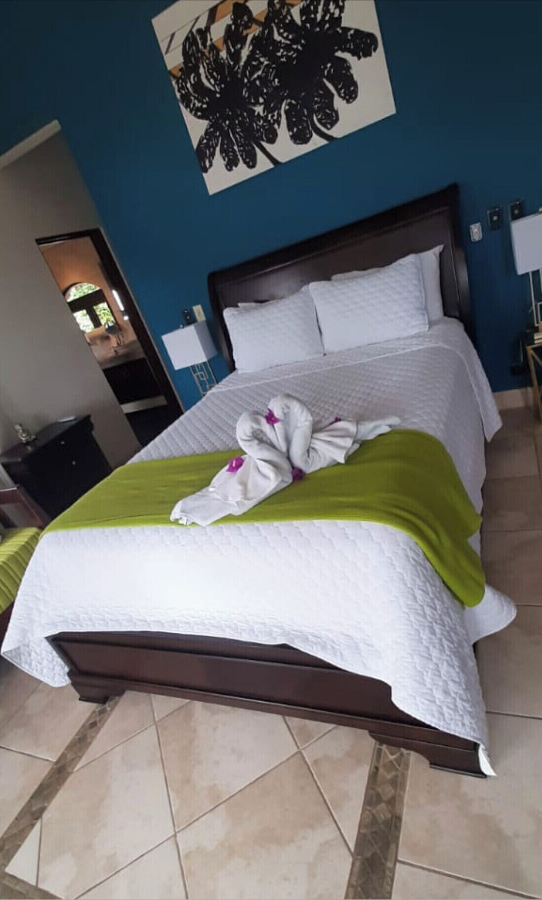 Un lit bien fait, avec un plaid vert et une serviette disposée en forme de nœud sur le lit.