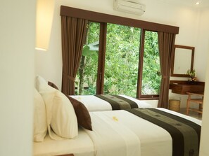 A hotel room with two beds, a wooden desk, a mirror, and large windows with curtains. - Eden House Ubud (Ubud)