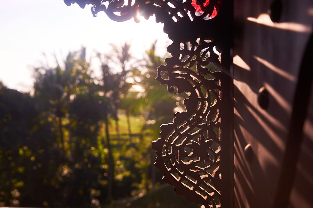 Une porte en métal décorative, ornée de motifs complexes, se dressant sur un fond de verdure et d’un ciel dégagé.