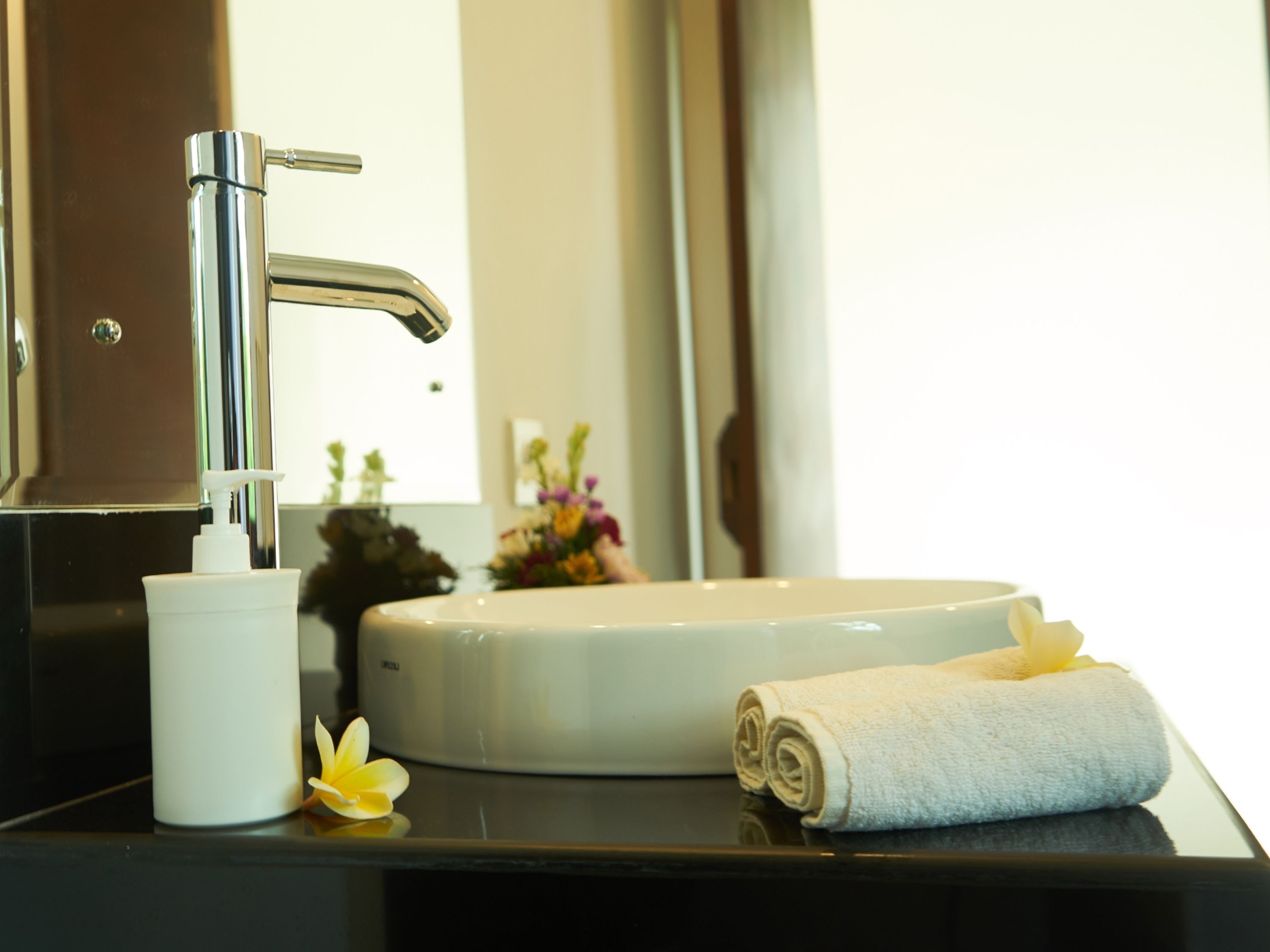 A bathroom sink with a chrome faucet, a white soap dispenser, and a rolled white towel on the counter.