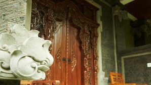 En dør i træ med detaljerede udskæringer, en stenskulptur og to træstole.