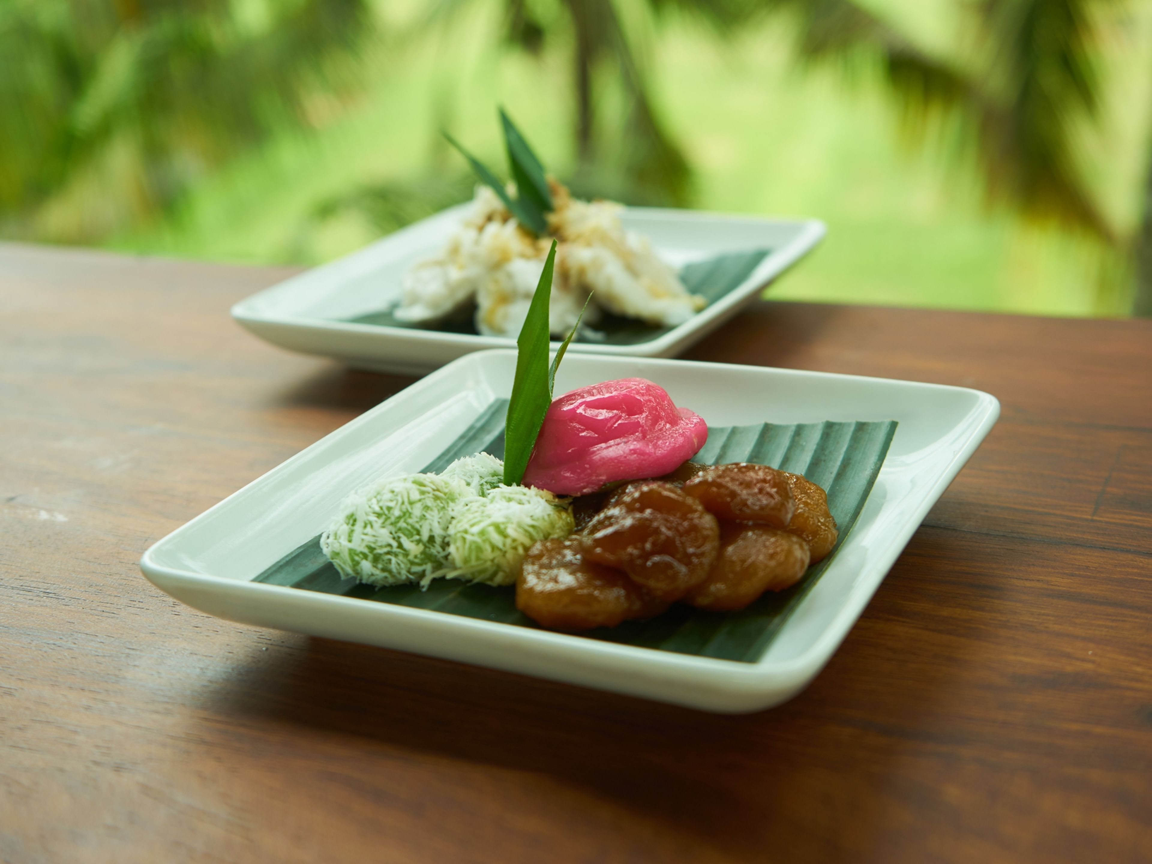 Two square plates with food on a wooden table.