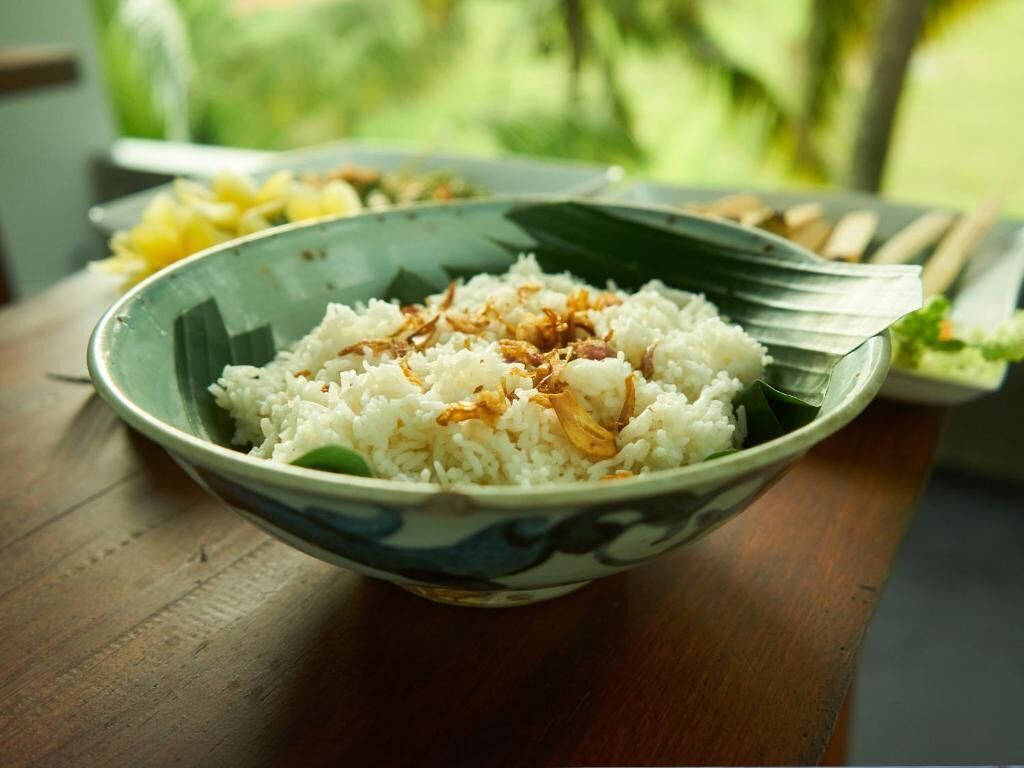 A bowl of white rice with fried onions on a wooden table.