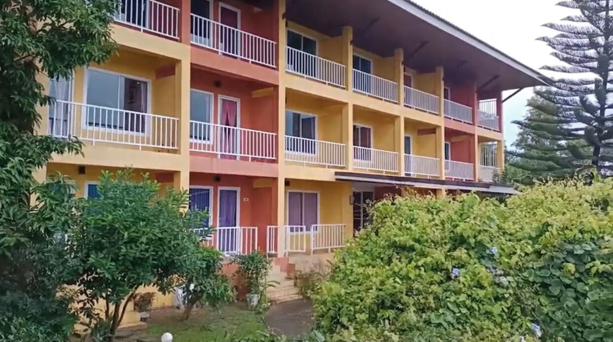 A multi-story building with balconies and a garden area in front.