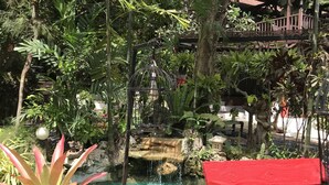 Un jardín con una pequeña cascada, plantas en macetas y un banco rojo.