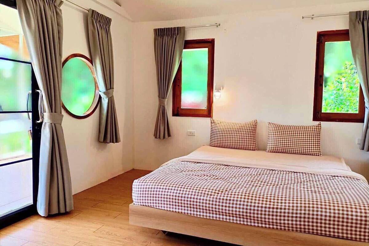A bedroom with a bed, curtains, a window, and a mirror.