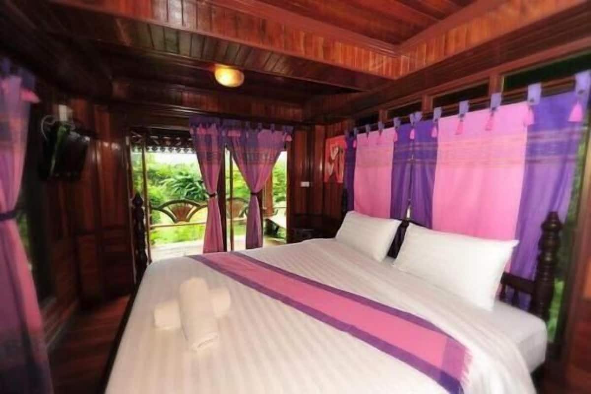A room with a bed, wooden walls, and a view of greenery.