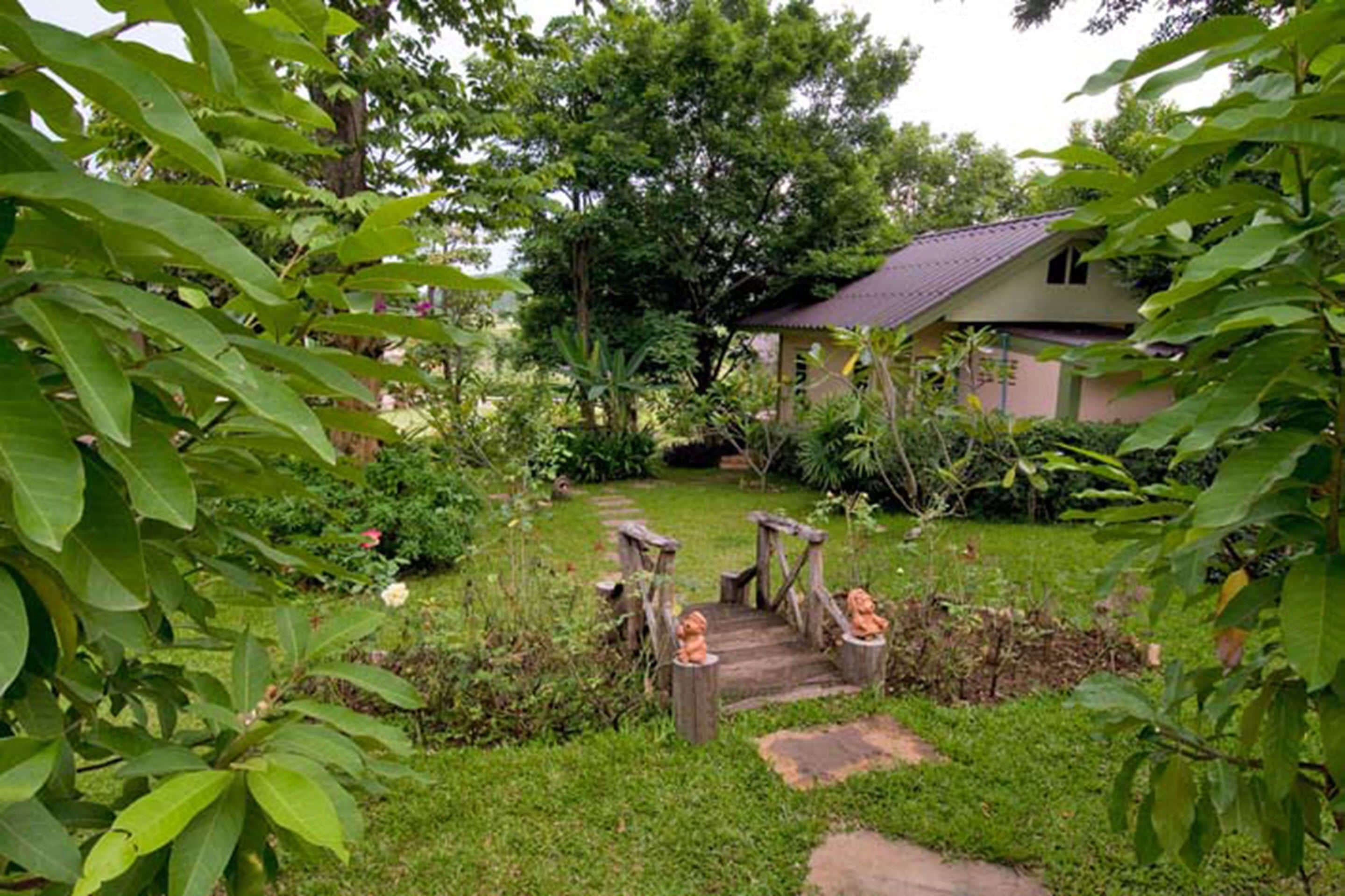 A garden with a wooden bridge, a small house, and lush greenery.
