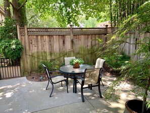 A patio with a round table and four chairs, surrounded by a wooden fence and lush greenery. - Quiet, Beautiful, East Sacramento Oasis - Walk to Coffee, Restaurants and Shops (SACRAMENTO)