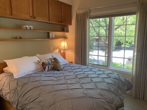 A bedroom with a large bed, a window with curtains, wooden cabinets above the bed, and a nightstand with a lamp. - Quiet, Beautiful, East Sacramento Oasis - Walk to Coffee, Restaurants and Shops (SACRAMENTO)