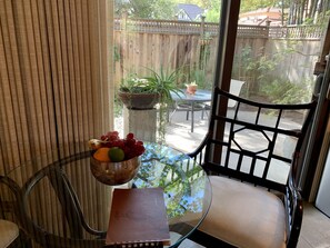 A glass table with a bowl of fruit, a notebook, and a chair in a room with a view of a wooden fence and greenery outside. - Quiet, Beautiful, East Sacramento Oasis - Walk to Coffee, Restaurants and Shops (SACRAMENTO)