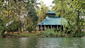 A building with a green roof, surrounded by dense greenery and a body of water. - Amritara Riverside Camp, Thattekad (Kothamangalam)