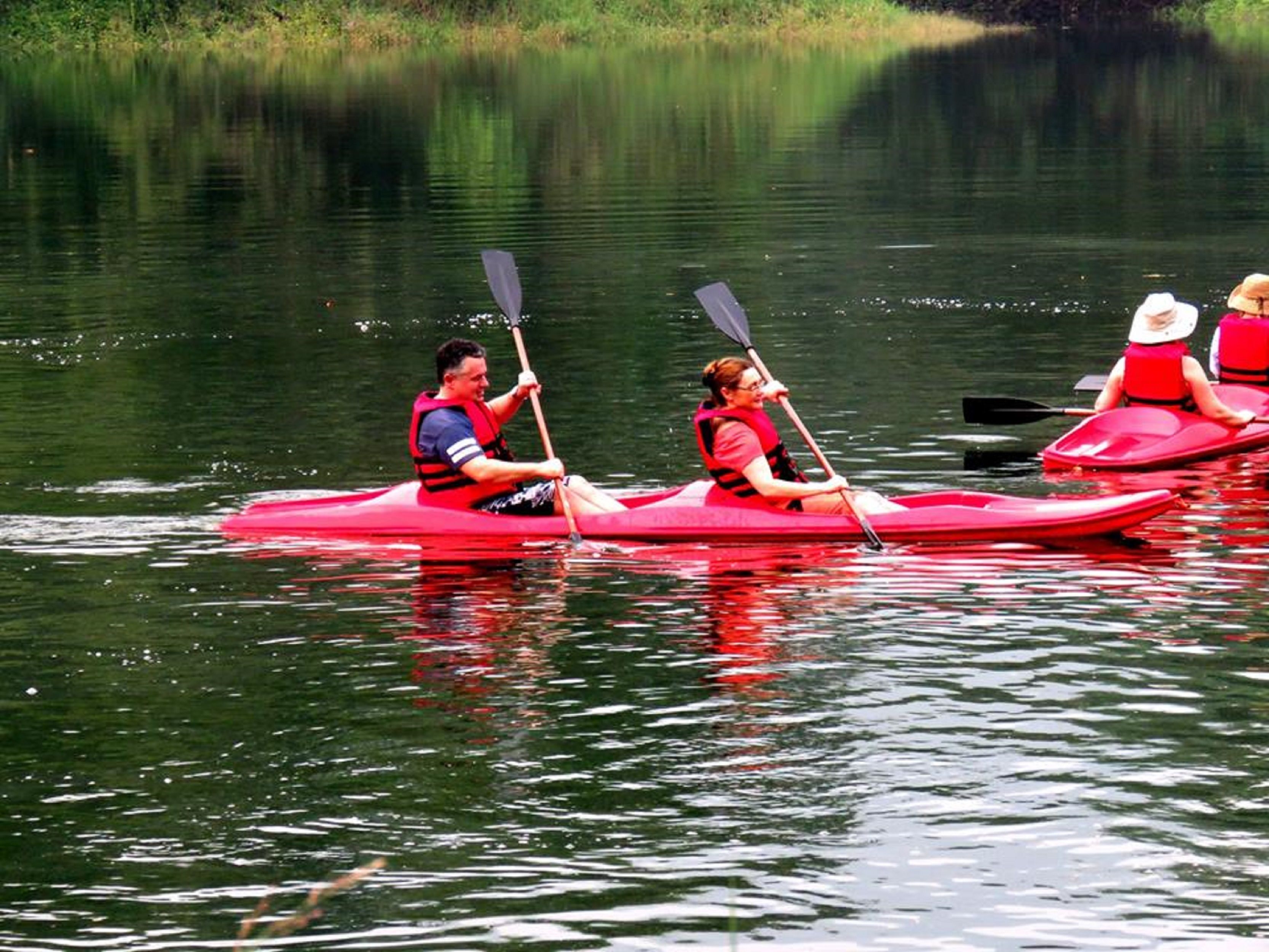 Drei Personen paddeln auf einem ruhigen See.