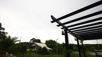 Un espacio exterior cubierto con un pérgola, una valla blanca y abundante vegetación.