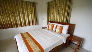 Una cama bien hecha con cabecera de madera, una mesita de noche y cortinas con estampado de hojas.