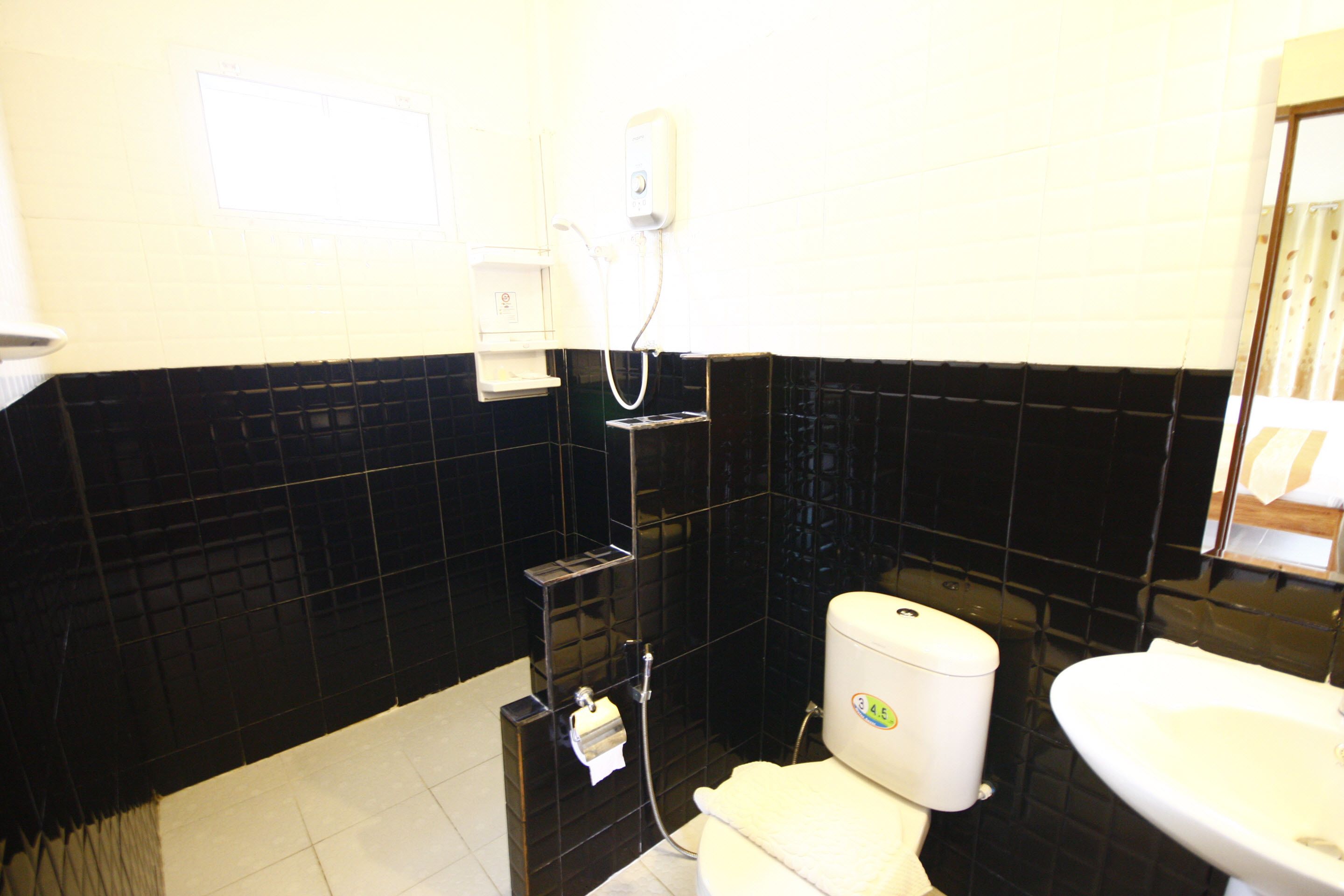 Un baño con paredes de azulejos blancos y negros, un inodoro, un lavabo y una ducha con cabezal de ducha manual.